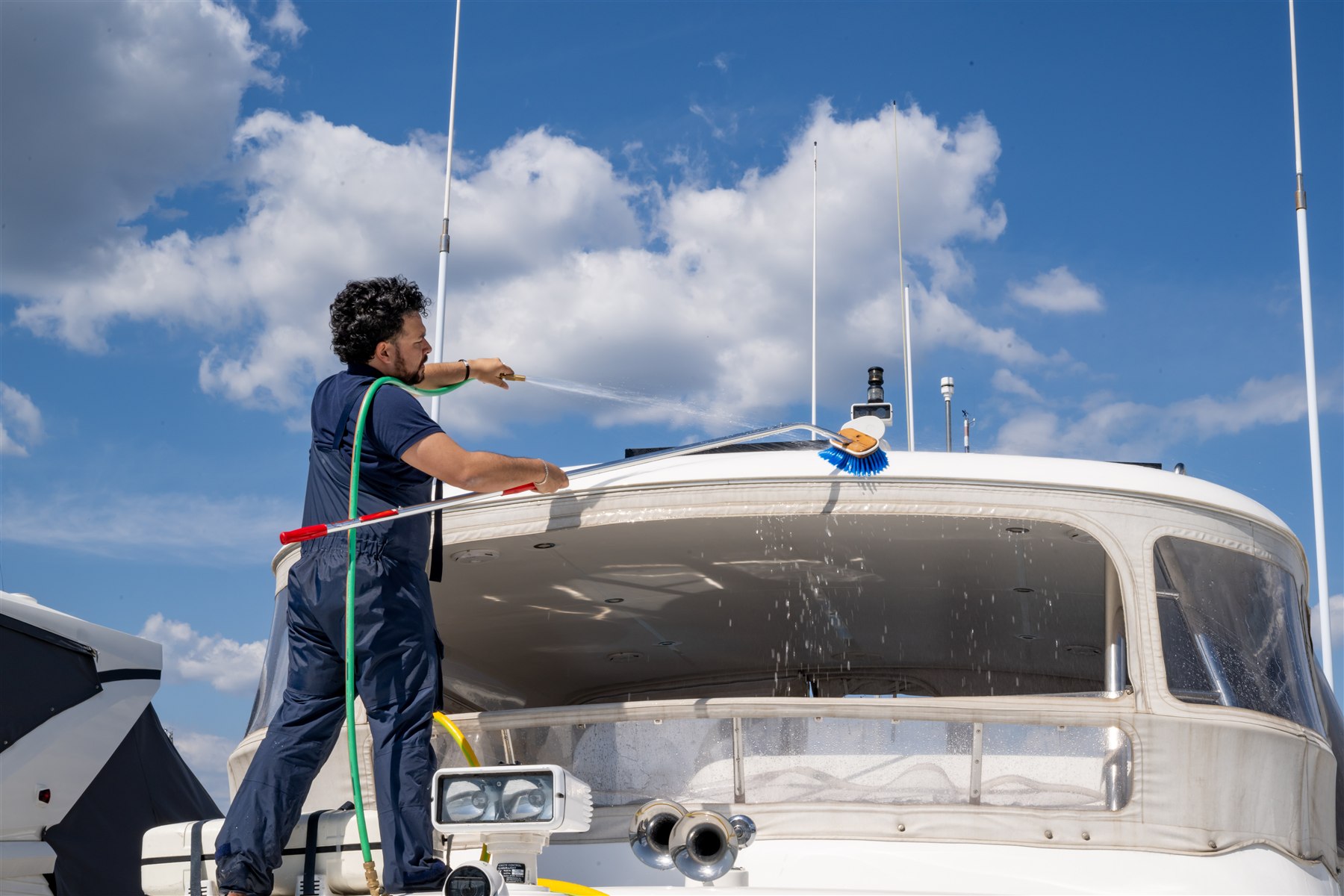 A marine service professional washing a white motor yacht